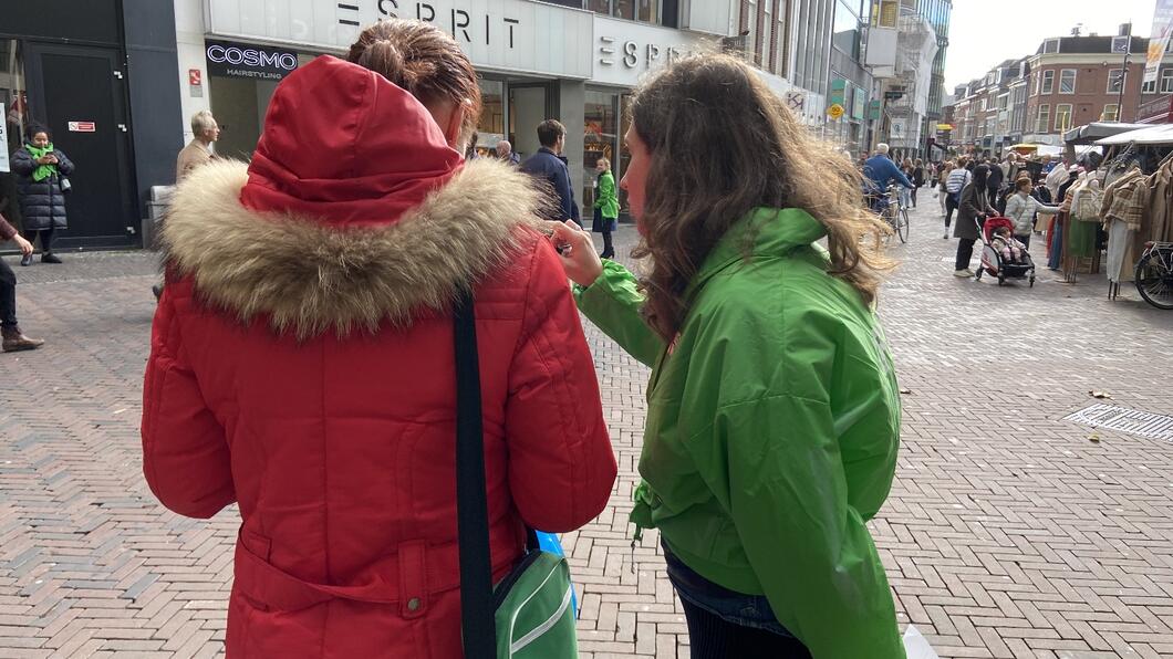 Iemand van GroenLinks is in gesprek met een inwoner van Utrecht op het Vredenburg tijdens de markt